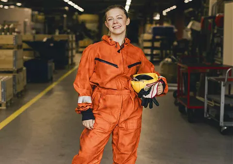 Une femme en combinaison orange, avec un casque jaune et des gants de protection dans une main