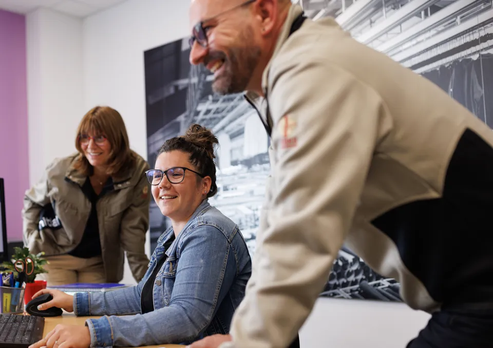 3 personnes souriantes qui regardent des écrans d'un même bureau