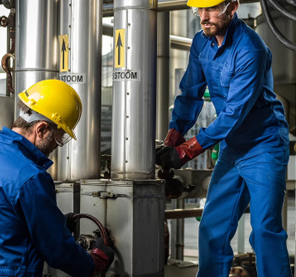 Deux personnes portant des EPI bleu, avec casques jaune, lunettes de protection et gant